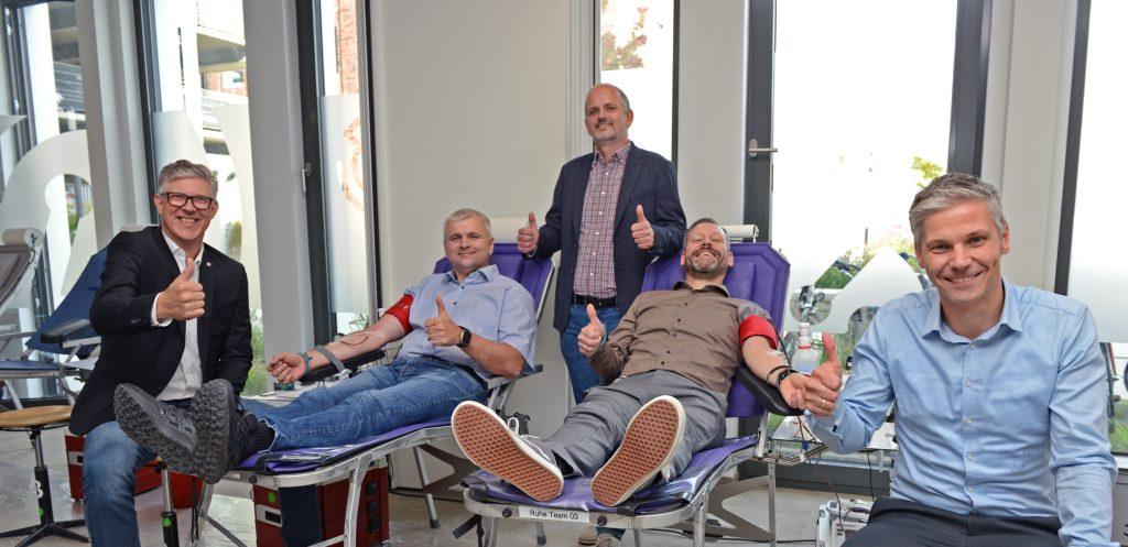 Four men sitting on chairs, smiling and giving thumbs up.